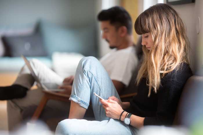 Ett ungt par sitter i en soffa med laptop och mobiltelefon.