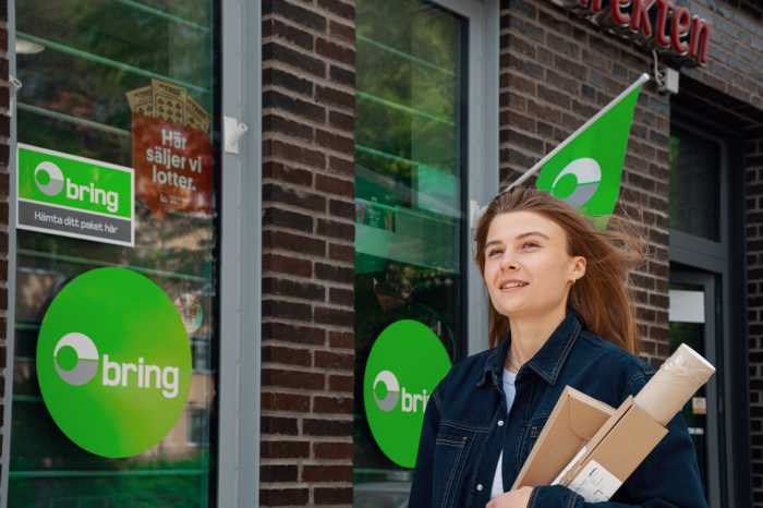 En kvinna går med paket i famnen utanför ett Bring paketombud