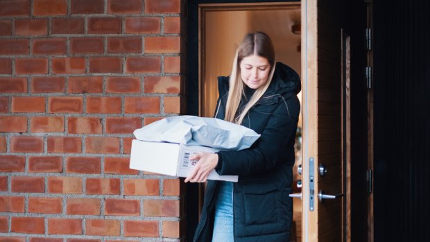En kvinna går ut genom en ytterdörr med flera paket i handen som ska returneras