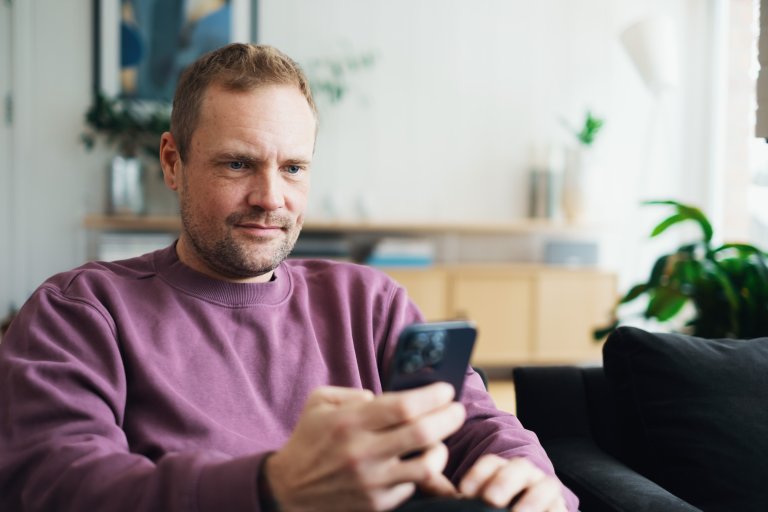 En man sitter och tittar på en mobiltelefon som han håller i handen