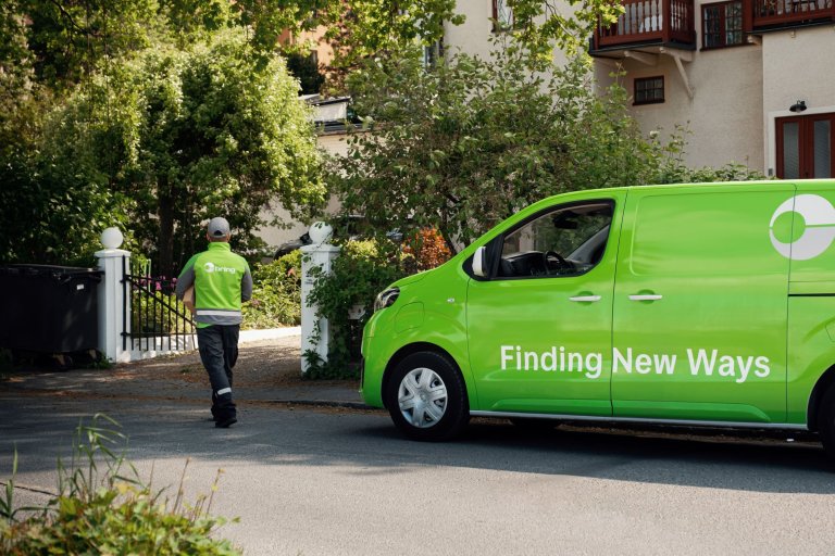 En Bringchaufför går framför en Bringbil mot ett hus för att leverera ett paket