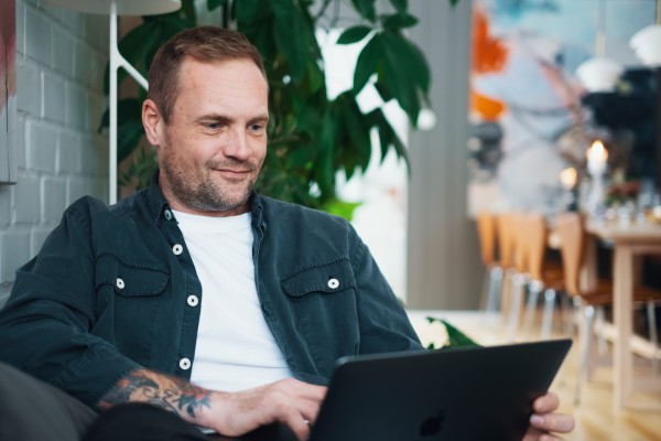 En man sitter på en soffa med en laptop i knät