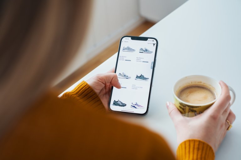 En kvinna har en mobil i handen med en webbutik som säljer skor