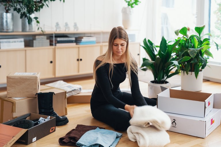 En kvinna sitter på golvet omgiven av massor av paket och produkter