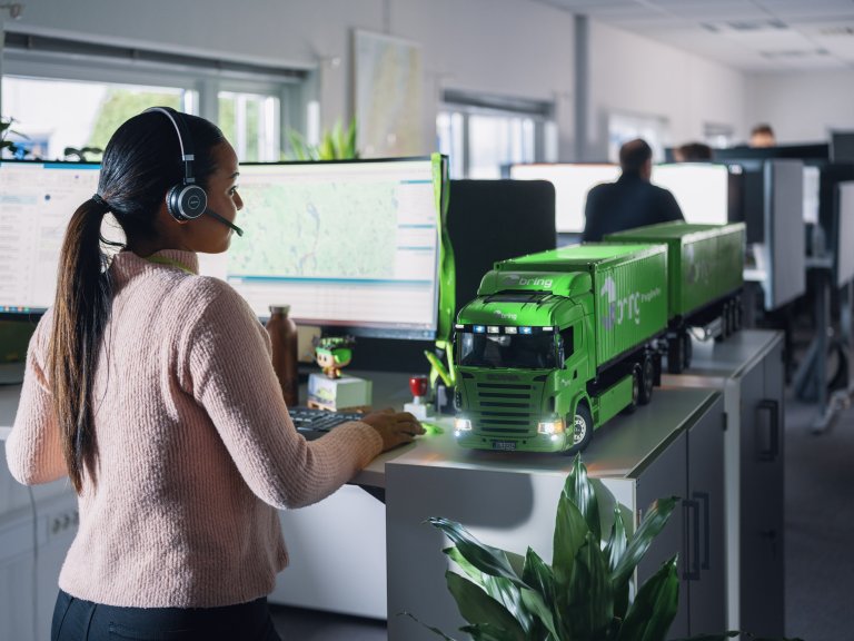 En kvinnlig medarbetare på Bring kundservice står med headset på sig framför en dataskärm