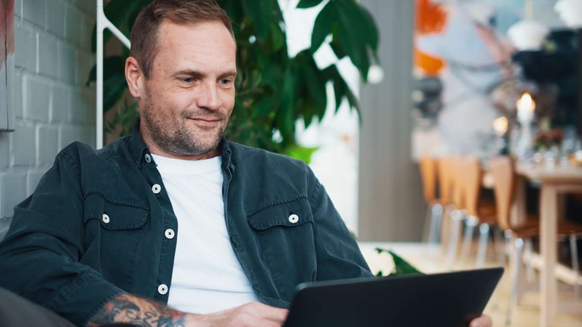 En man sitter på en soffa med en laptop i knät och handlar på nätet