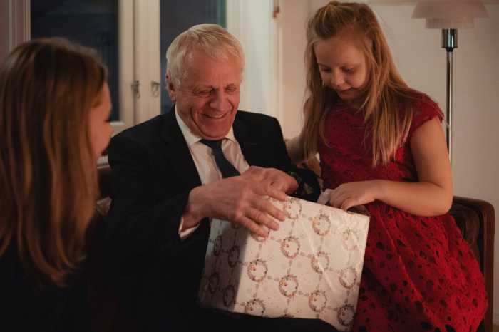 Äldre man sitter med familjen och öppnar en julklapp som är köpt i en nätbutik.