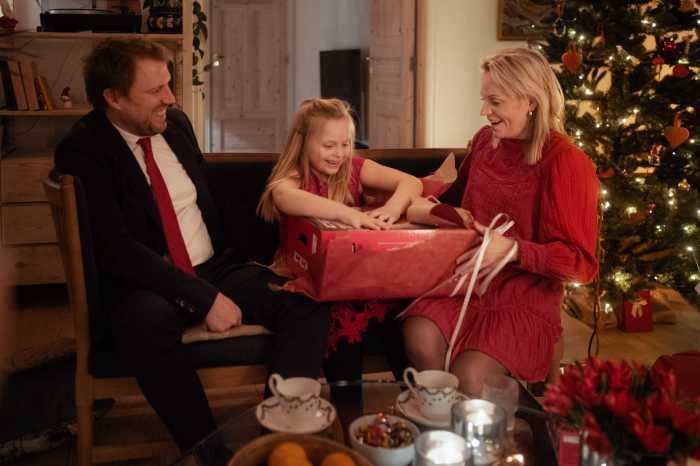 Ett barn sitter mellan en man och en kvinna på julafton och öppnar en julklapp som är köpt i en webbutik