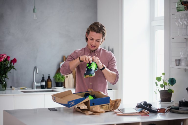 En man står vid en bänk och håller i en sko som han har handlat i en webbutik.