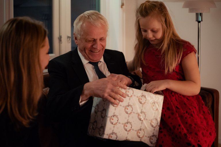 En äldre man sitter på en soffa med sitt barnbarn bredvid och öppnar en julklapp som är köpt i en webbutik.