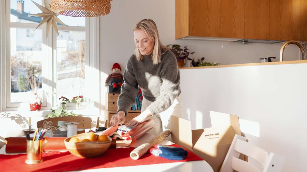 En leende kvinna står lutad över ett bord medan hon slår in en julklapp som hon har handlat på Black Friday