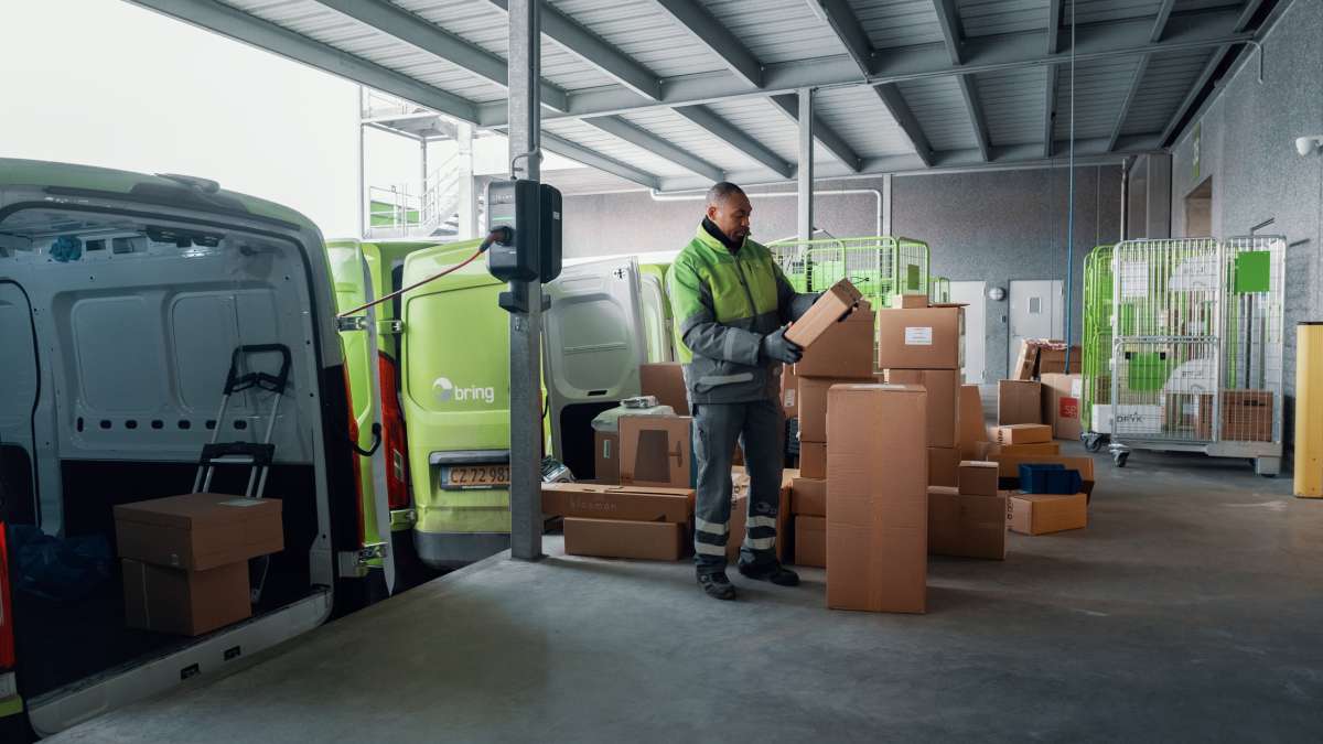 En Bring chaufför står med ett paket i handen bredvid andra paket på en terminal