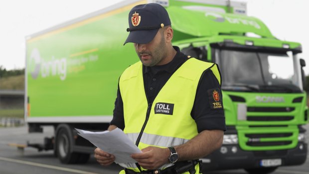 Tulltjänsteman kontrollerar dokument framför en grön Bring leveransbil.